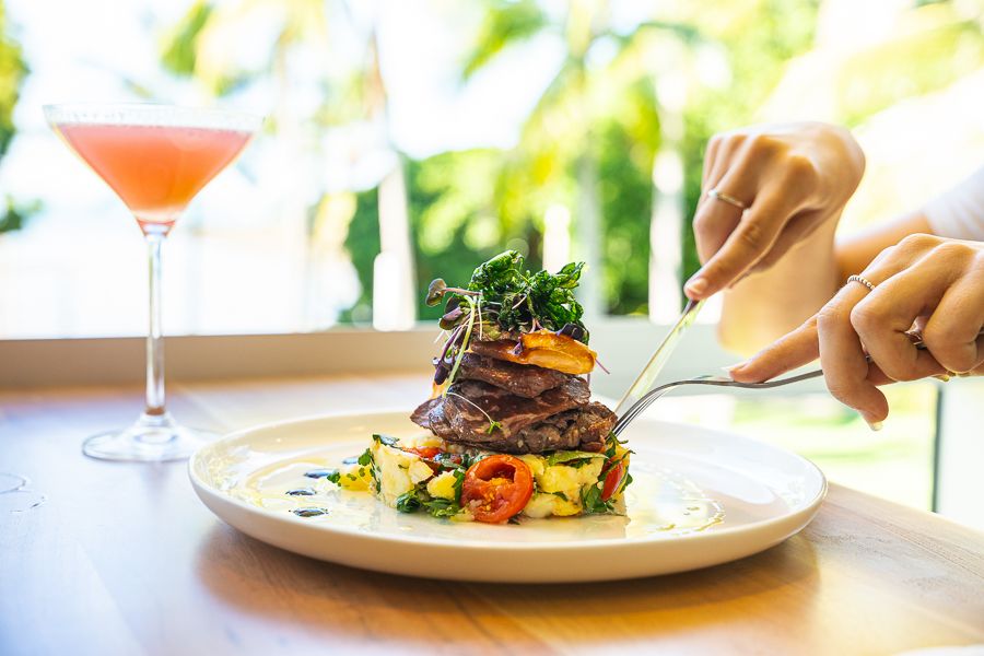 a plate with a stack of vegetables and meat with hands cutting into it