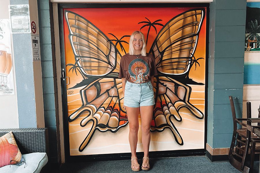 Girl with blonde hair standing in front of a painting of butterfly wings