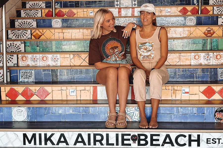 Two girls sitting on a set of colourful mosaic tiled stairs