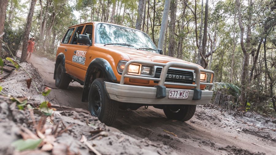 orange 4wd driving through the rainforest on k'gari