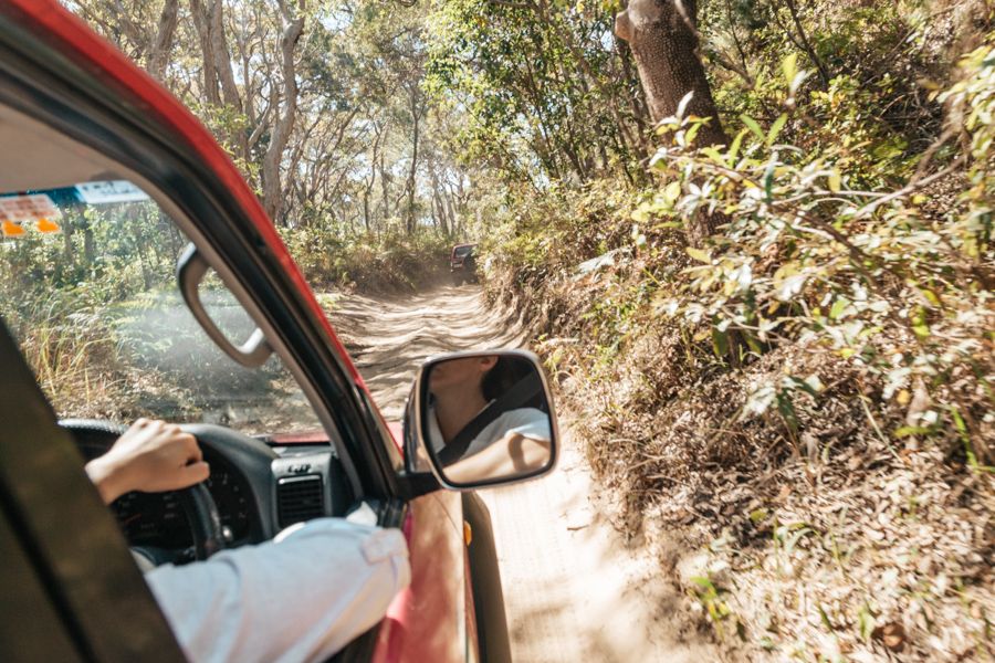 person driving a 4wd through a sandy forest track on k'gari