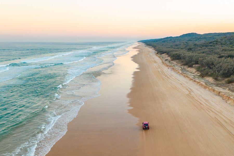 pink 4wd driving on the k'gari coastline next to ocean