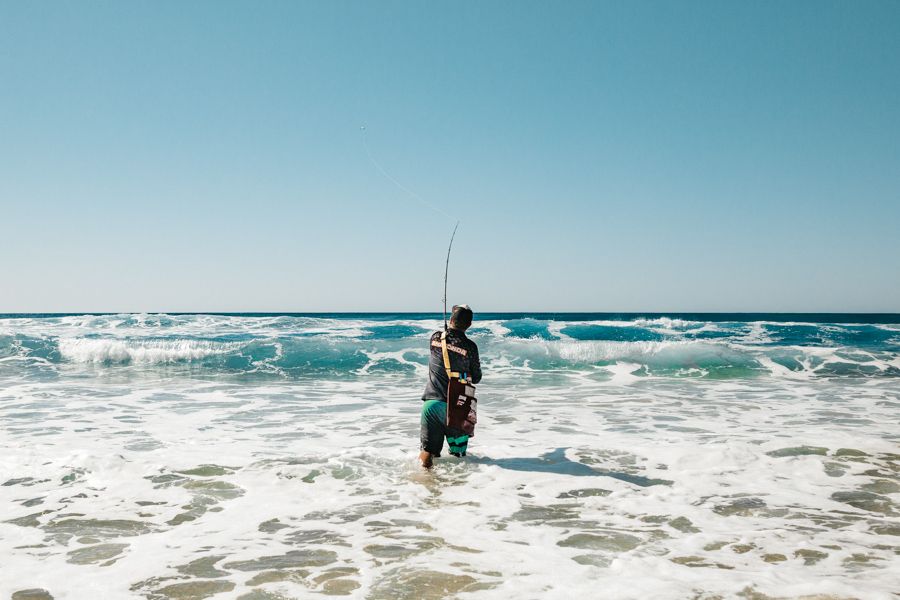 man throwing a fishing line into the ocean on K'gari beach