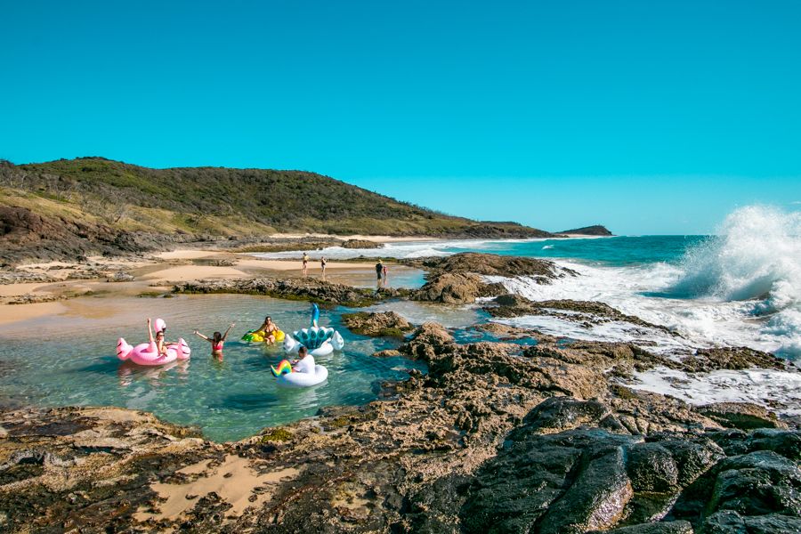 people floating on colorful floats in a rock pool near the beach