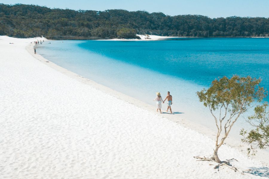 couple walking hand in hand on the shores of lake mckenzie