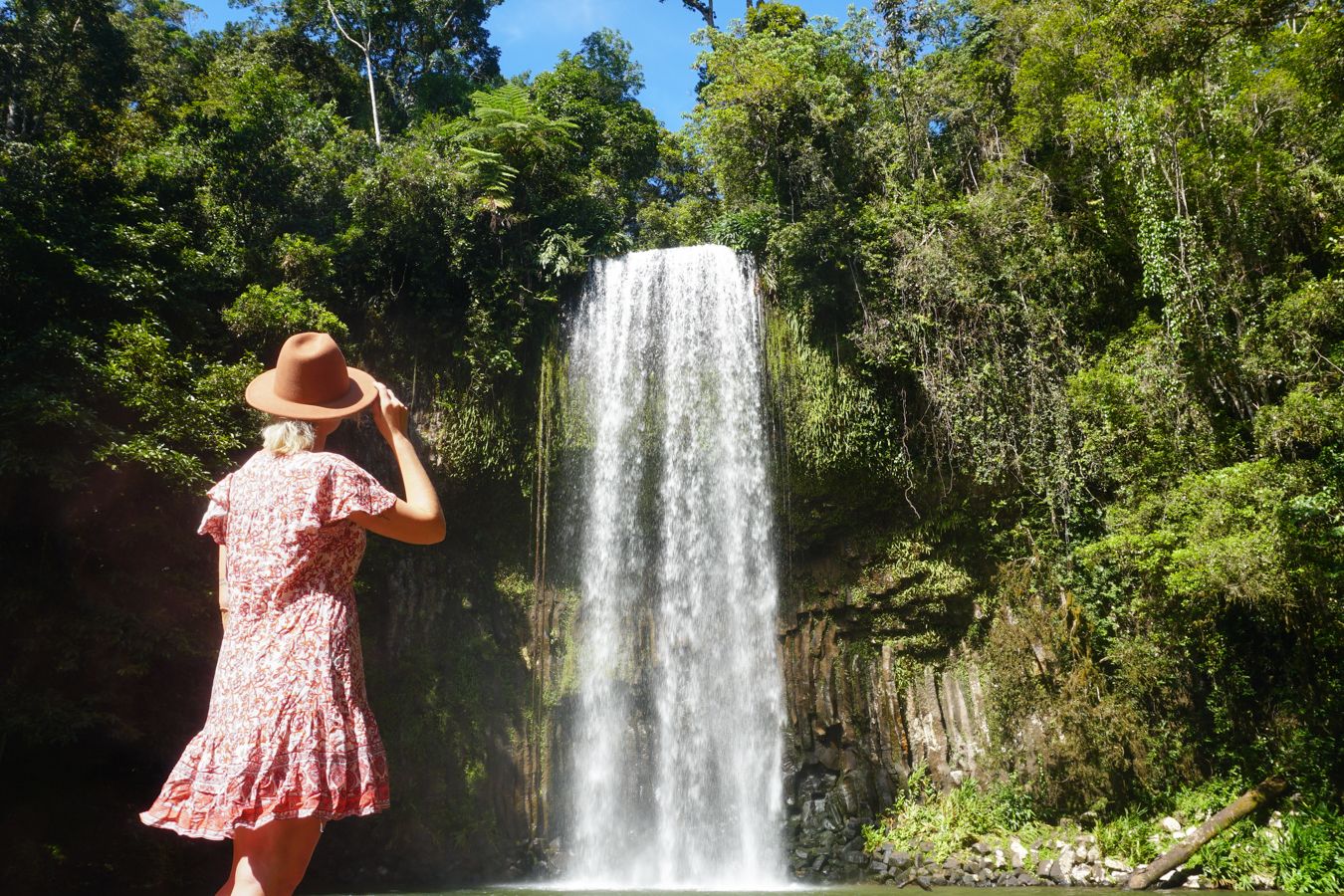 Girl with red dress standing in front of a waterfall