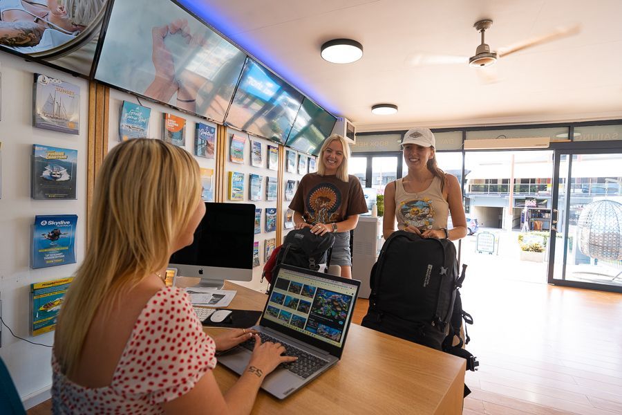 Two girls smiling at another girl sitting behind a desk in a shop