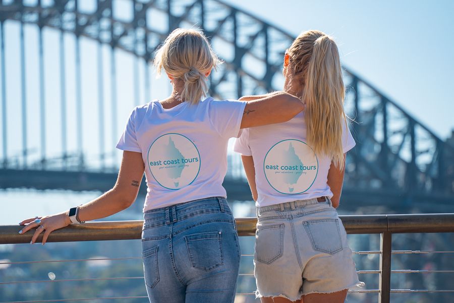 Two blonde girls wearing white shirts looking out at the Sydney Harbour Bridge