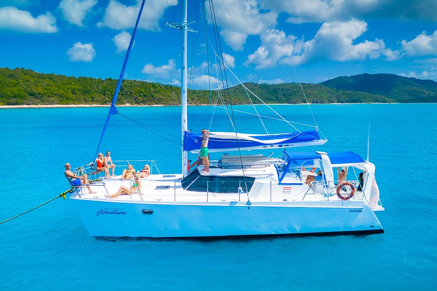 a drone shot of a catamaran at bay with people on the front deck