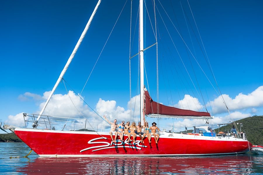 a group of people sitting on the edge of a red sail boat