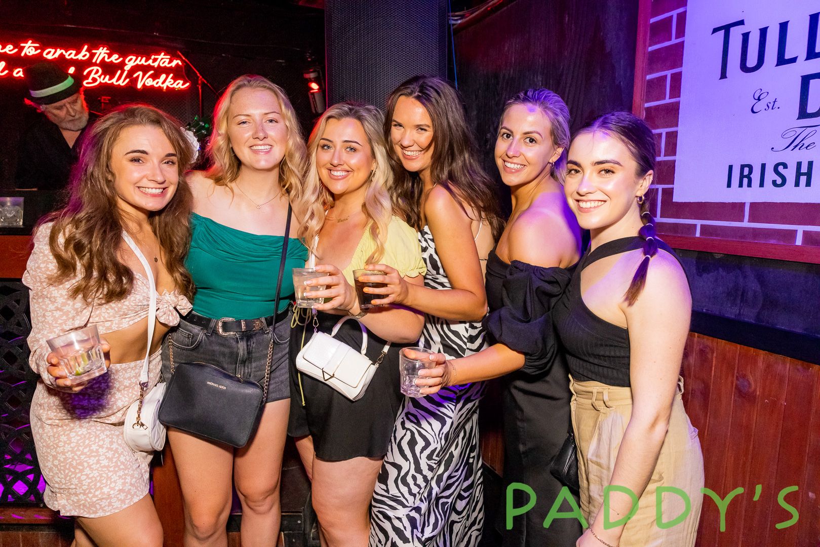 A group of girls standing together on a dance floor with drinks in hands