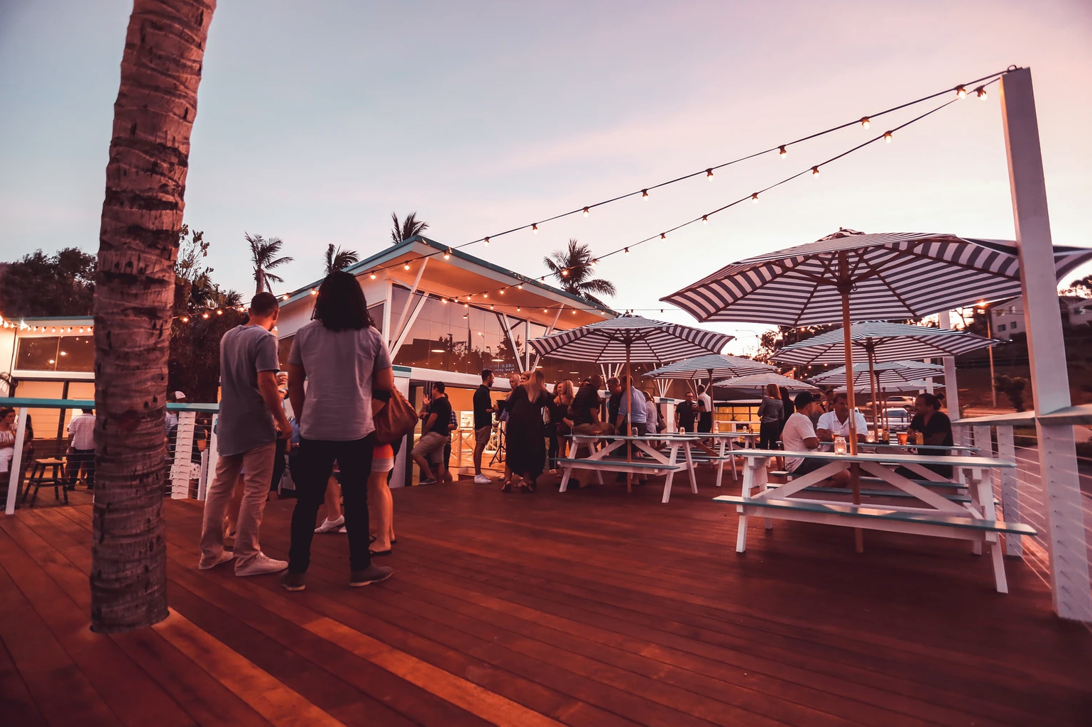 The outdoor area of a bar with people gathered around tables and chairs