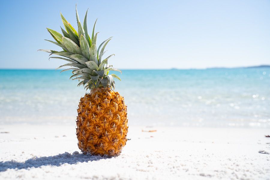 A pineapple sitting on a white sand beach