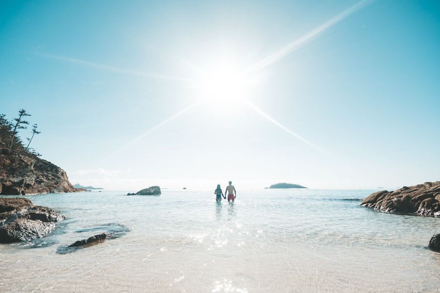 Couple holding hands go for a swim at Whitehaven Beach, Whitsundays