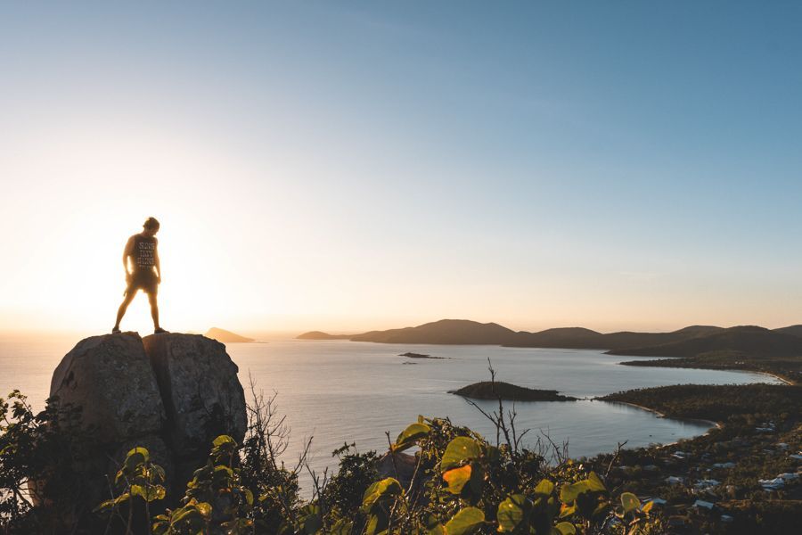 Man stands on large rock at the summit of Hydeaway Bay watching the sunrise