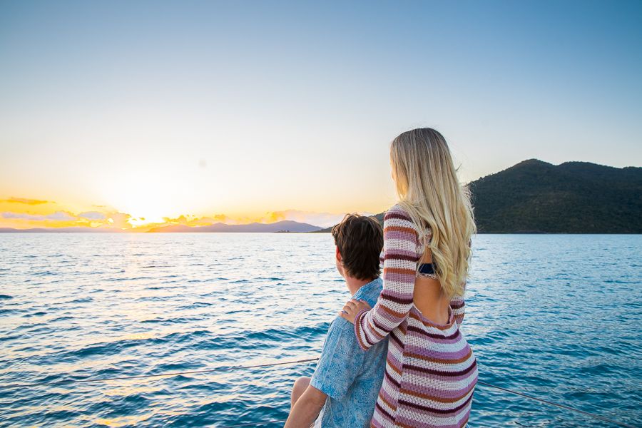 a man and woman on a boat sailing at sunset
