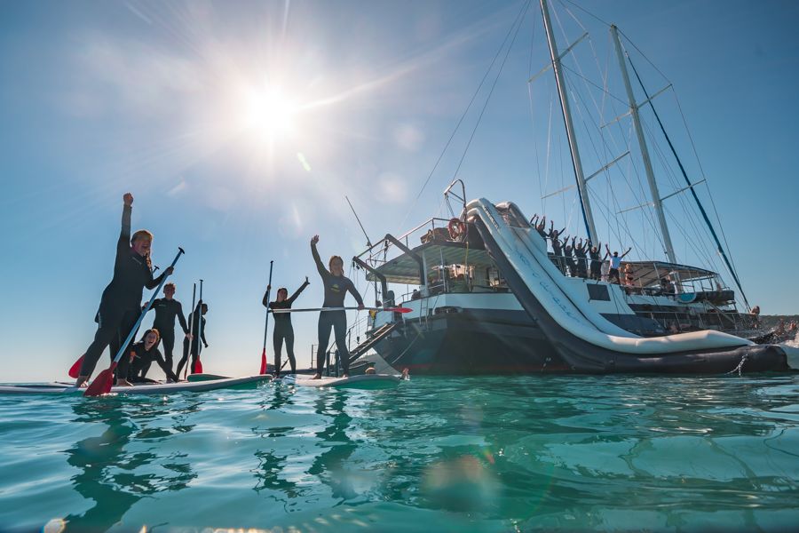 People on stand-up paddleboards in front of Atlantic Clipper, Whitsundays