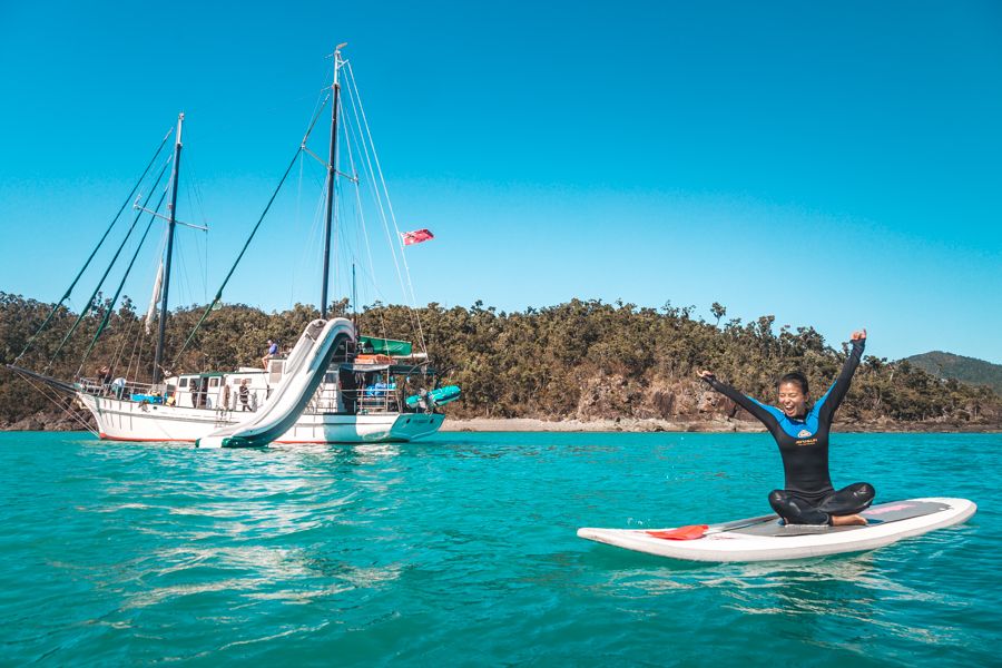 Person wearing a stinger suit on a SUP in the Whitsundays, New Horizon vessel moored in the background