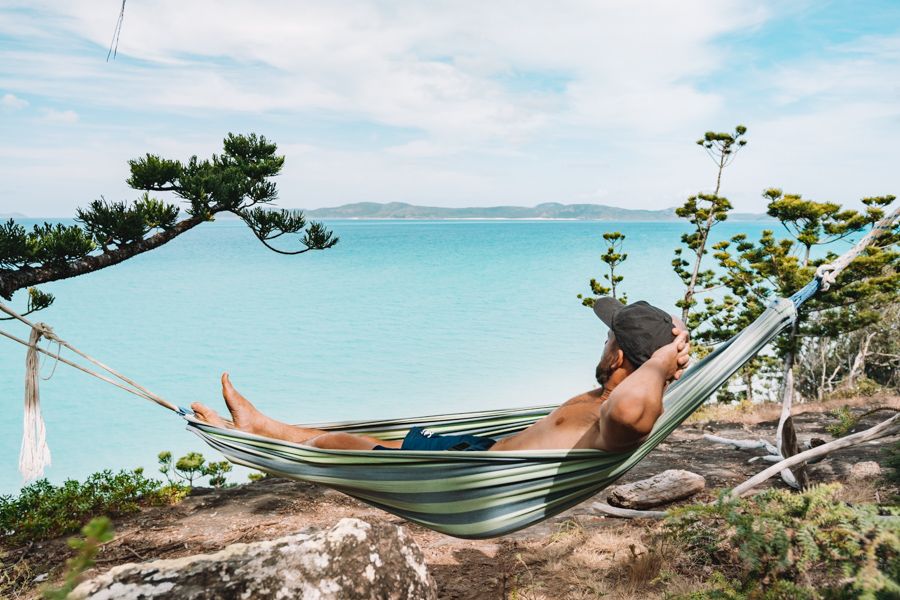 Man wearing a cap sitting in a hammock overlooking the Whitsundays