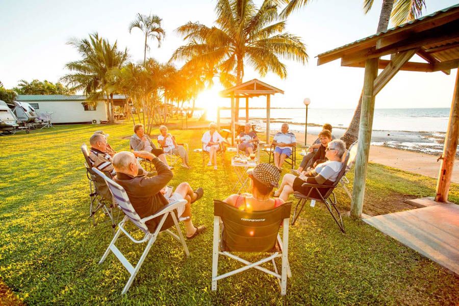 A group of people sitting in camping chairs on the waters edge of a caravan park