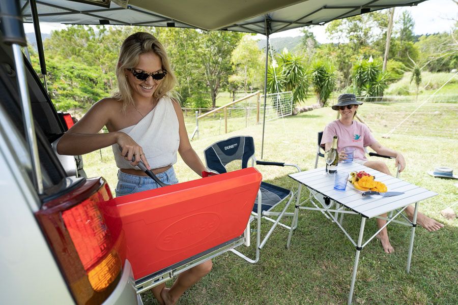 A couple cooking and relaxing by their caravan under an awning