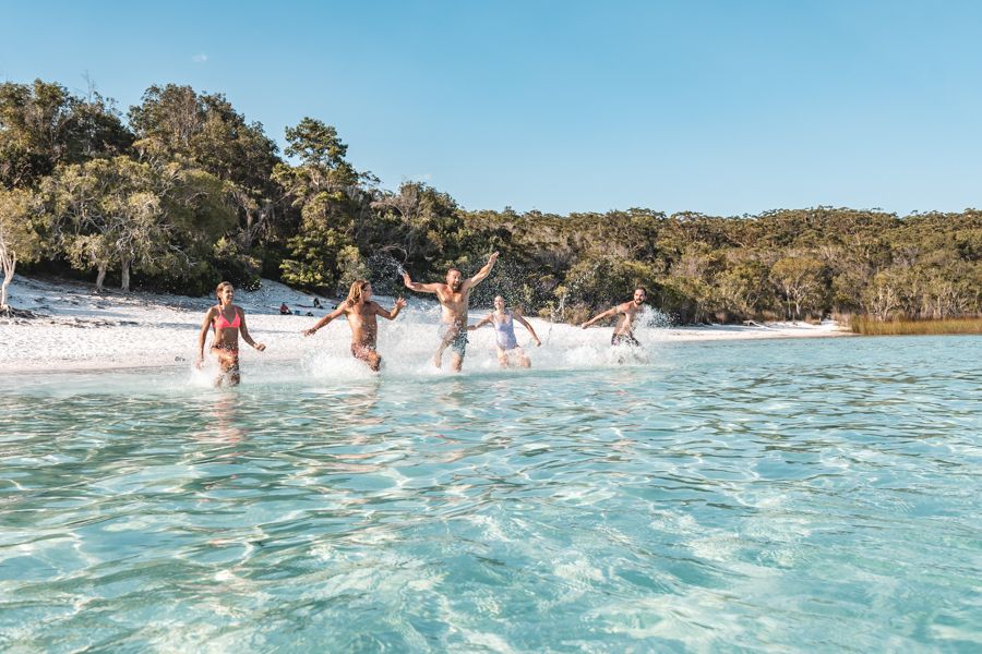 Backpackers running into the crystal clear waters of Lake McKenzie