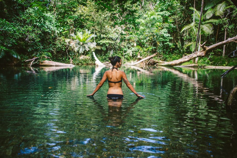 Woman standing amongst rainforest in a waterfall pool