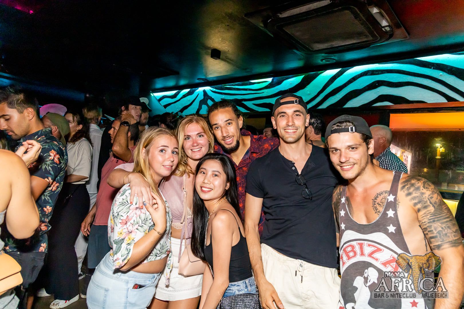 A group of males and females posing for a photo in a dimly lit nightclub