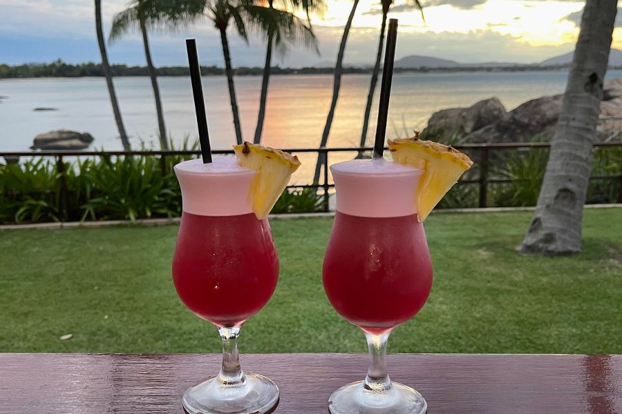 Two red coloured cocktails with the sunset in the background