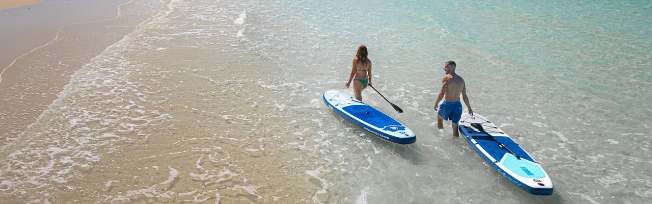 Paddle Boarding A drone shot of a man and woman walking along the beach carrying paddle boards