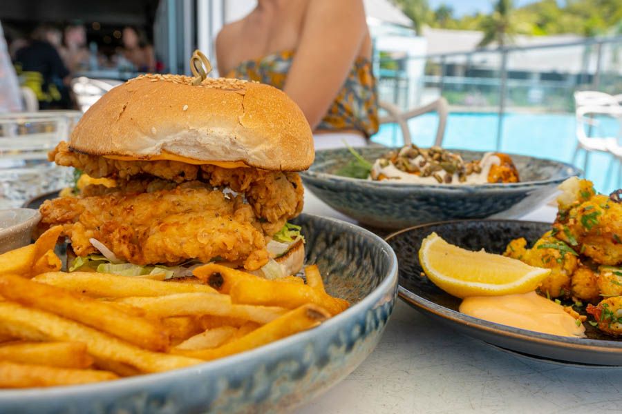 A hamburger and chips on a table with the ocean in the background