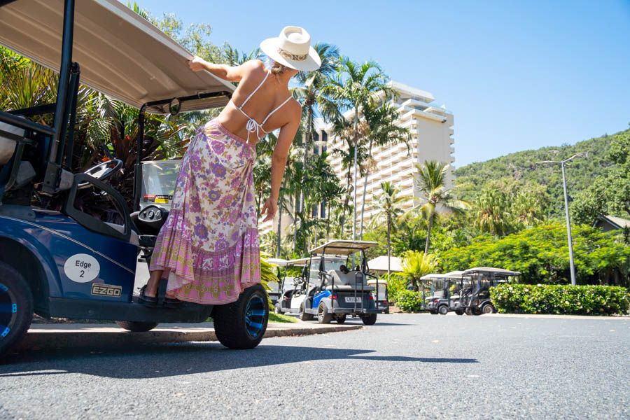 Blonde girl hanging off a golf buggy in front of a resort and palm trees