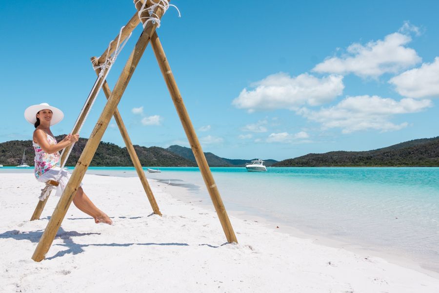 Girl sitting on a swing in white sand and tropical blue water 