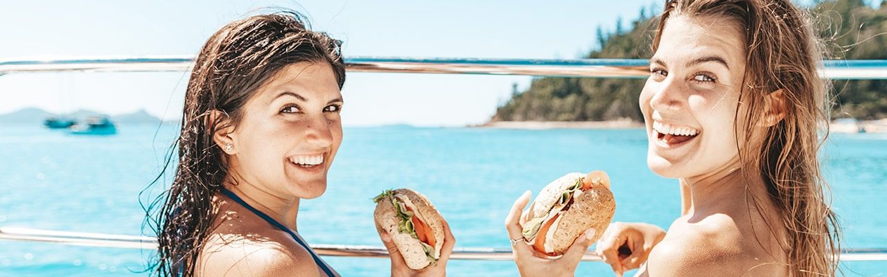 Two people eating bread and salad rolls on the foredeck of Powerplay