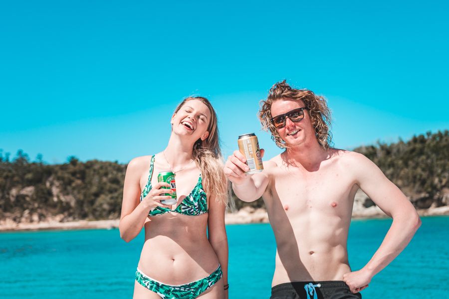 A man and woman standing in the water holding a can of beer each