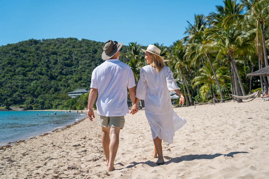 Couple wearing hats walking along Catseye Beach on Hamilton Island