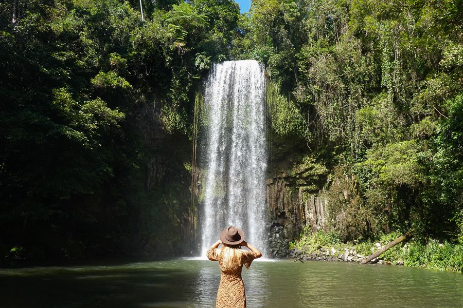 A girl in a brown hat standing in front of a waterfall