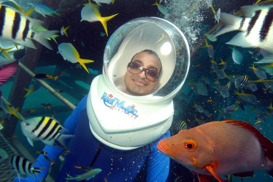 A man with a diving helmet on, underwater surrounded by fish