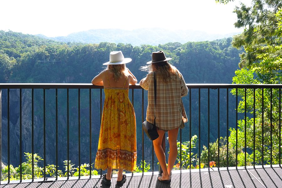 Two girls on viewing platform in foreground, Barron Falls in background, impressive waterfall cascading down mammoth rocky outcrop, sunny day