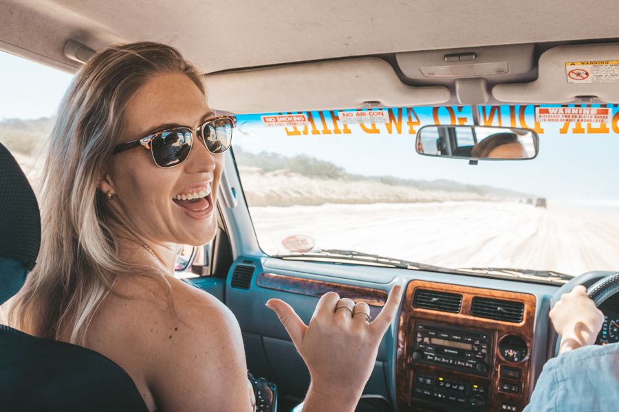 Women wearing sunglasses on a K'gari 4WD tour throwing a 'shakkas' sign 