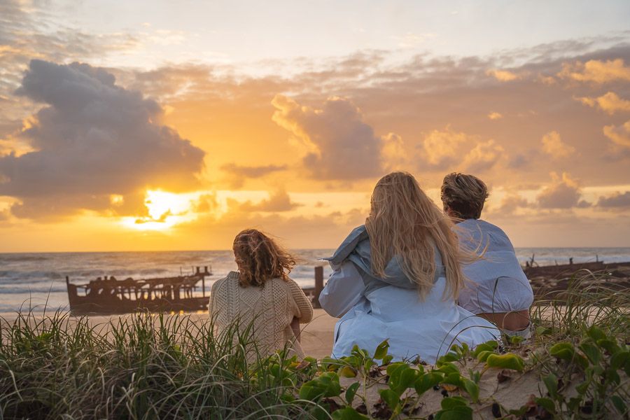 3 people watching the sunset against the backdrop of a shipwreck