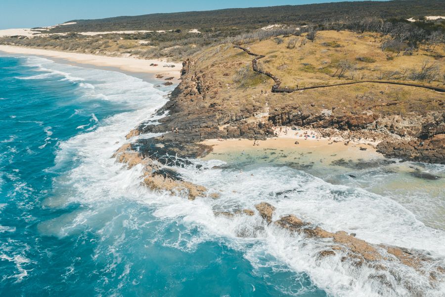 an aerial photo of a beach on K'gari with blue waters, sands and a headland