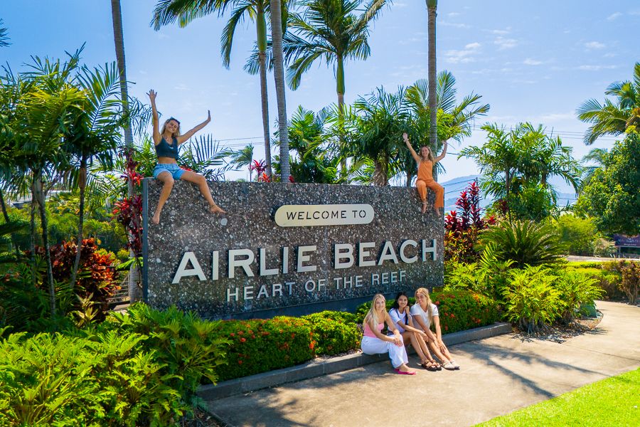 people posing in front of airlie beach sign