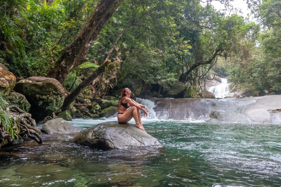 girl sitting near a cascading waterfall in the forest near Cairns