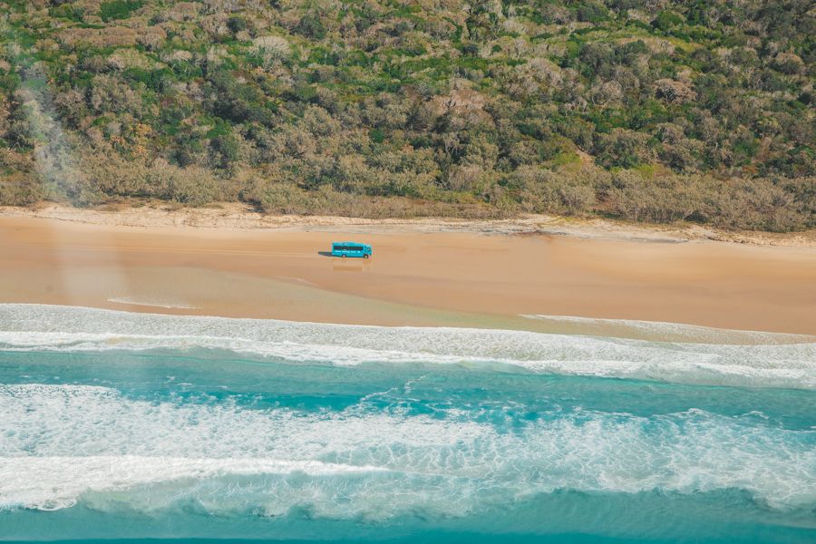 aerial view of blue bus driving on the sand at 75 mile beach