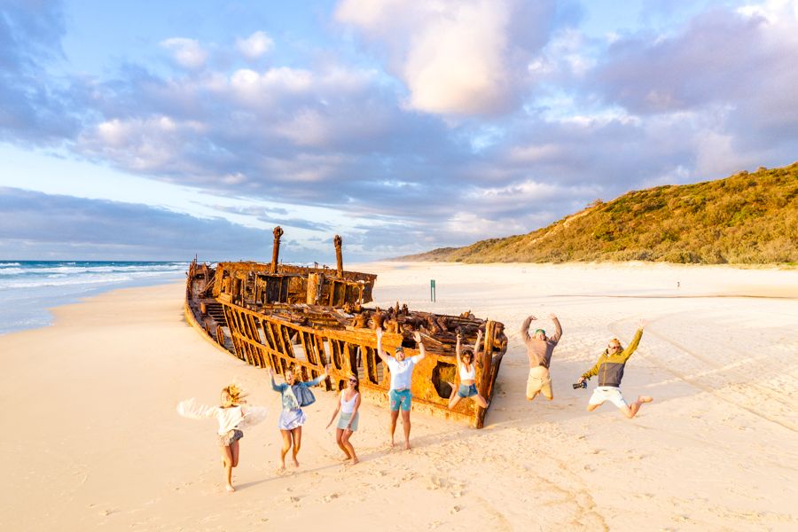 people jumping on the beach in front of Maheno Shipwreck