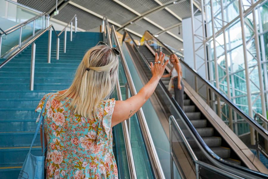 Two people waving goodbye to each other on the airport escalator