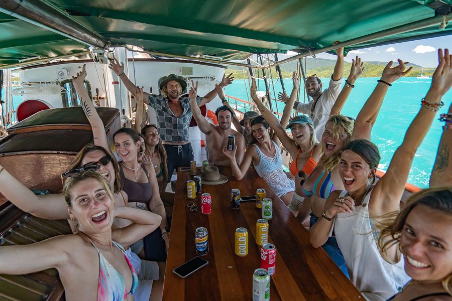 A group of people smiling and waving their hands in the air on board a boat