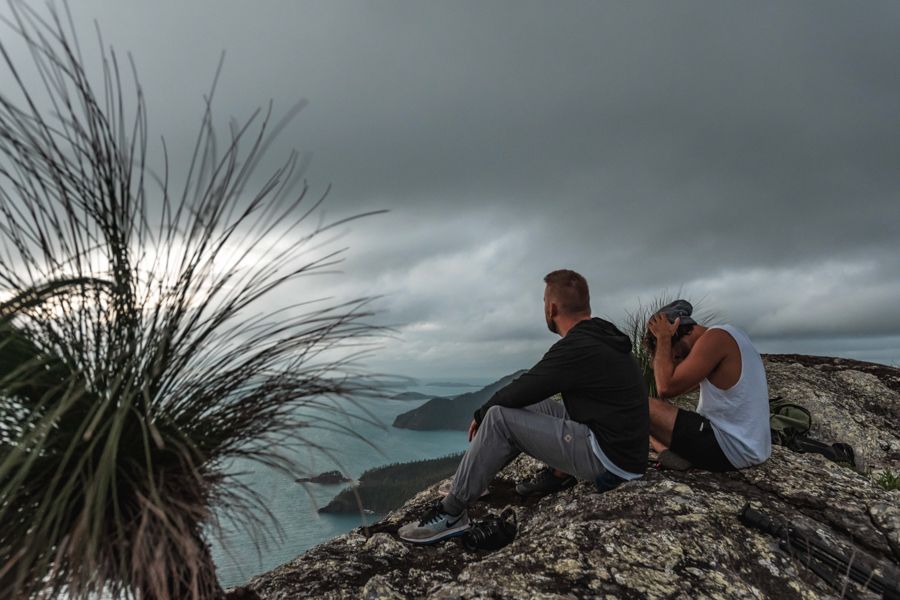 Two people sitting on a headland with dark grey clouds above