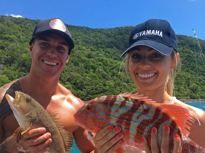 couple smiling while holding two fish on a fishing tour